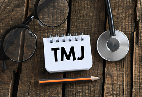 Notepad on a desk with TMJ written on it