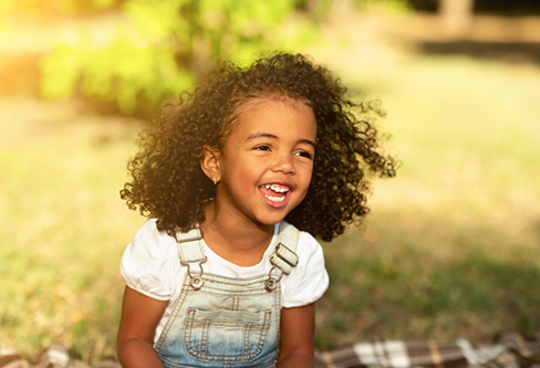 Young girl in overalls sitting in the grass on a sunny day