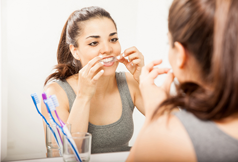 Woman putting on a teeth whitening strip in front of her bathroom mirror