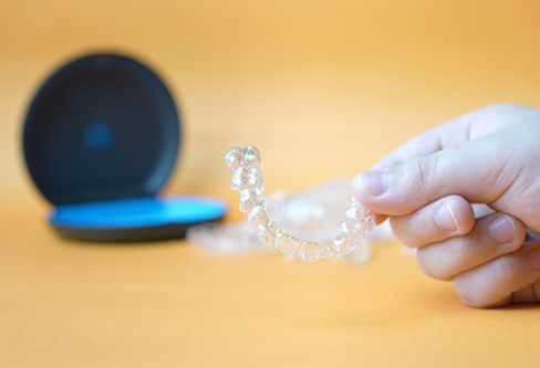 Hand holding an Invisalign clear aligner in front of its plastic storage case