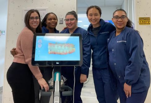 Doctor Sheng and the Stratford Smiles team smiling next to a wheeled monitor showing impressions of teeth