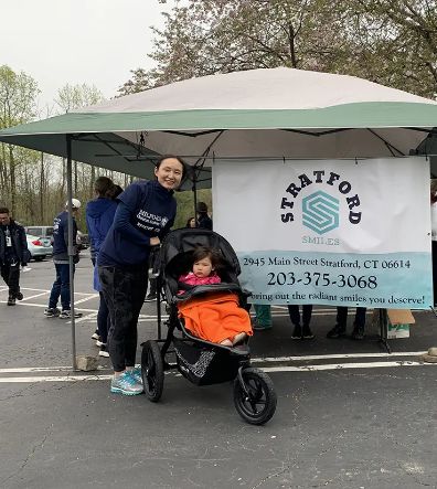 Doctor Sheng with a baby in a stroller by a Stratford Smiles table at a local event
