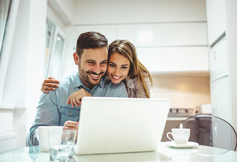 Smiling man and woman looking at a laptop on their kitchen table