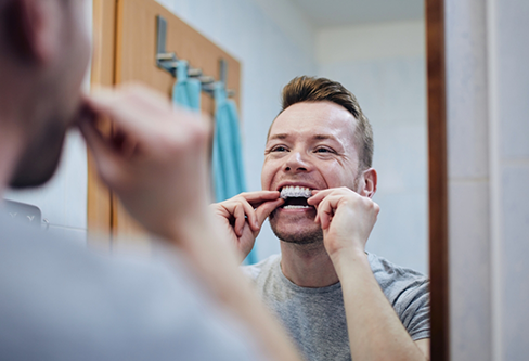 Man placing an at home teeth whitening tray over his teeth