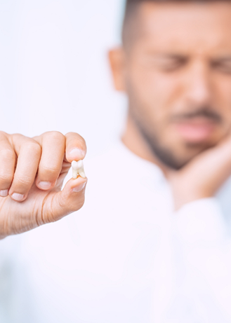 Man touching his face in pain while holding an extracted tooth