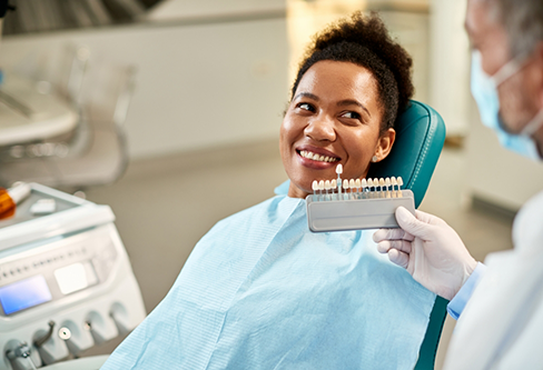 Dentist holding a row of veneers in front of a patient's smile